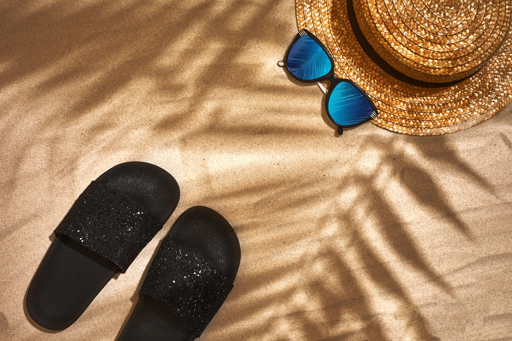 Chinelos de tira larga preto com glitter na areia da praia.