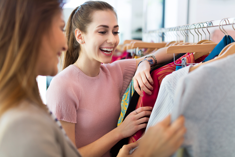 Vendedora sorrindo ao realizar a abordagem ao cliente e mostrar camisetas.