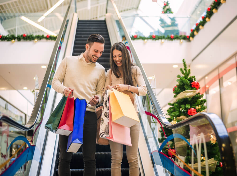 Casal hetero descendo escada rolante de shopping.