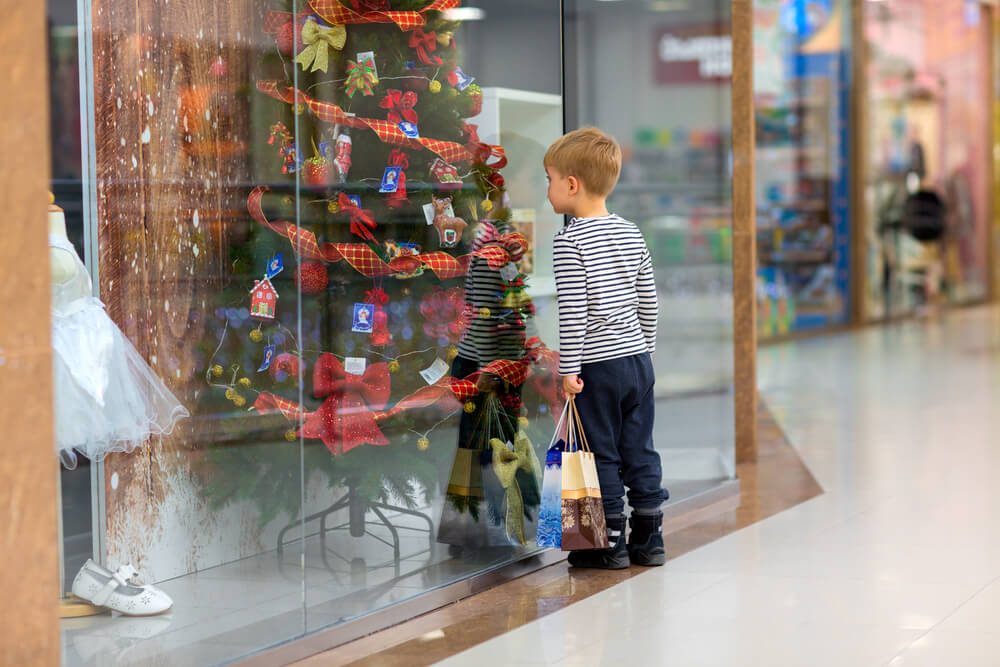 Criança olhando para vitrine da loja de calçados decorada para o Natal.